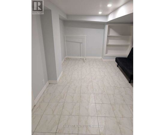 A spacious room with white tiled flooring and a black couch.