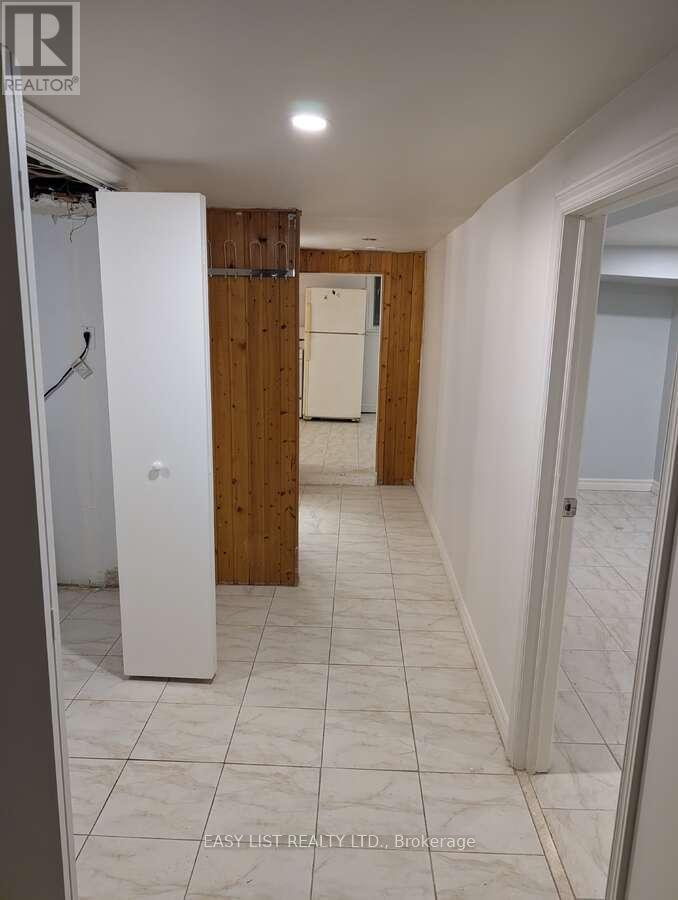 A white refrigerator stands in a kitchen with wooden walls and tile flooring.