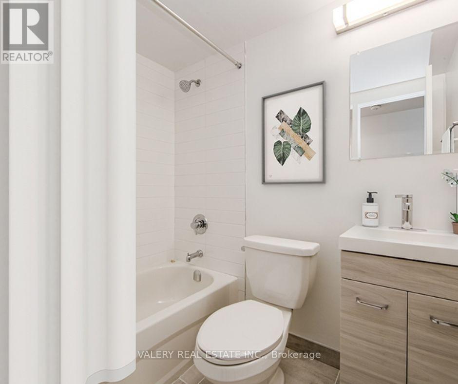 A white toilet in a bathroom with a framed picture of leaves on the wall.