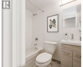 A white toilet in a bathroom with a framed picture of leaves on the wall.