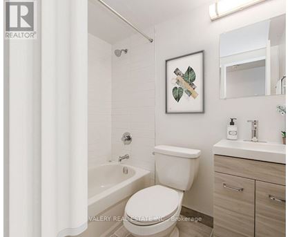 A white toilet in a bathroom with a framed picture of leaves on the wall.