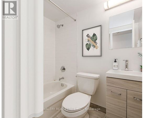 A white toilet in a bathroom with a framed picture of leaves on the wall.