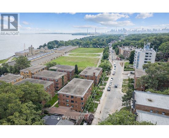 A bird's eye view of a residential area with apartment buildings, a parking lot, and a body of water in the background.
