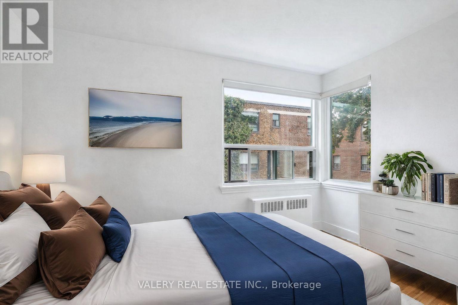 A bedroom with a bed, pillows, a nightstand, and a window with a view of a building.