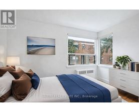 A bedroom with a bed, pillows, a nightstand, and a window with a view of a building.