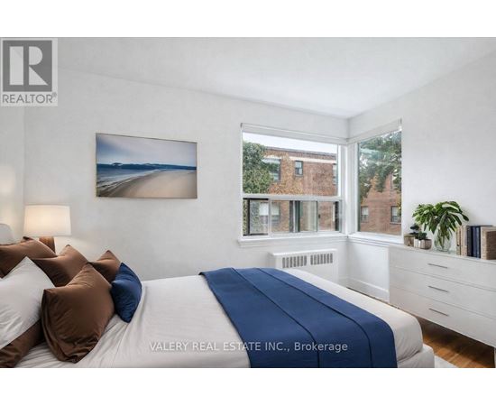 A bedroom with a bed, pillows, a nightstand, and a window with a view of a building.