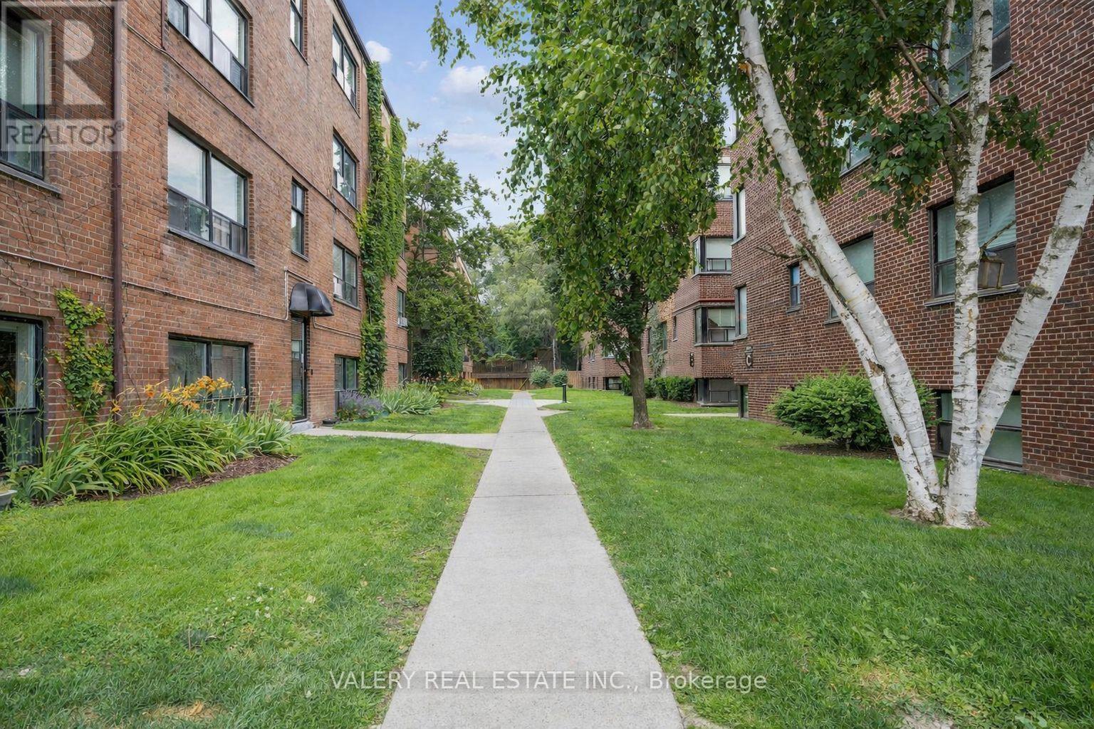 A tree-lined walkway leads between two rows of red brick apartment buildings.