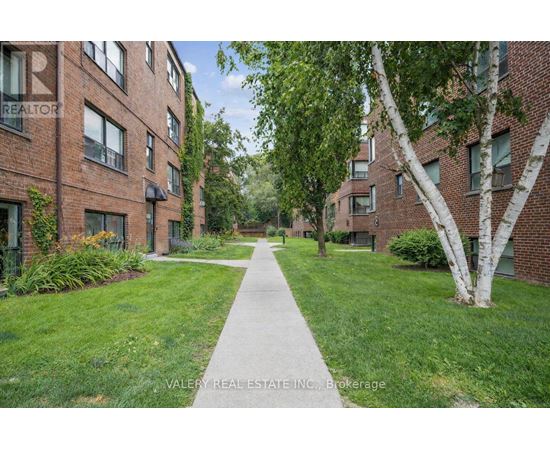 A tree-lined walkway leads between two rows of red brick apartment buildings.