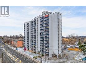 A tall residential building with a flat roof and a balcony on the top floor.