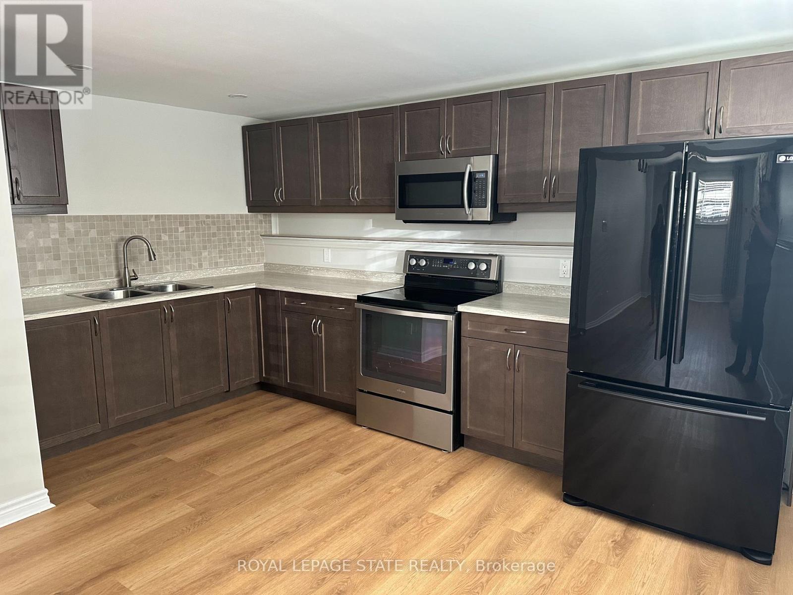 A kitchen with a black fridge and wooden floors.
