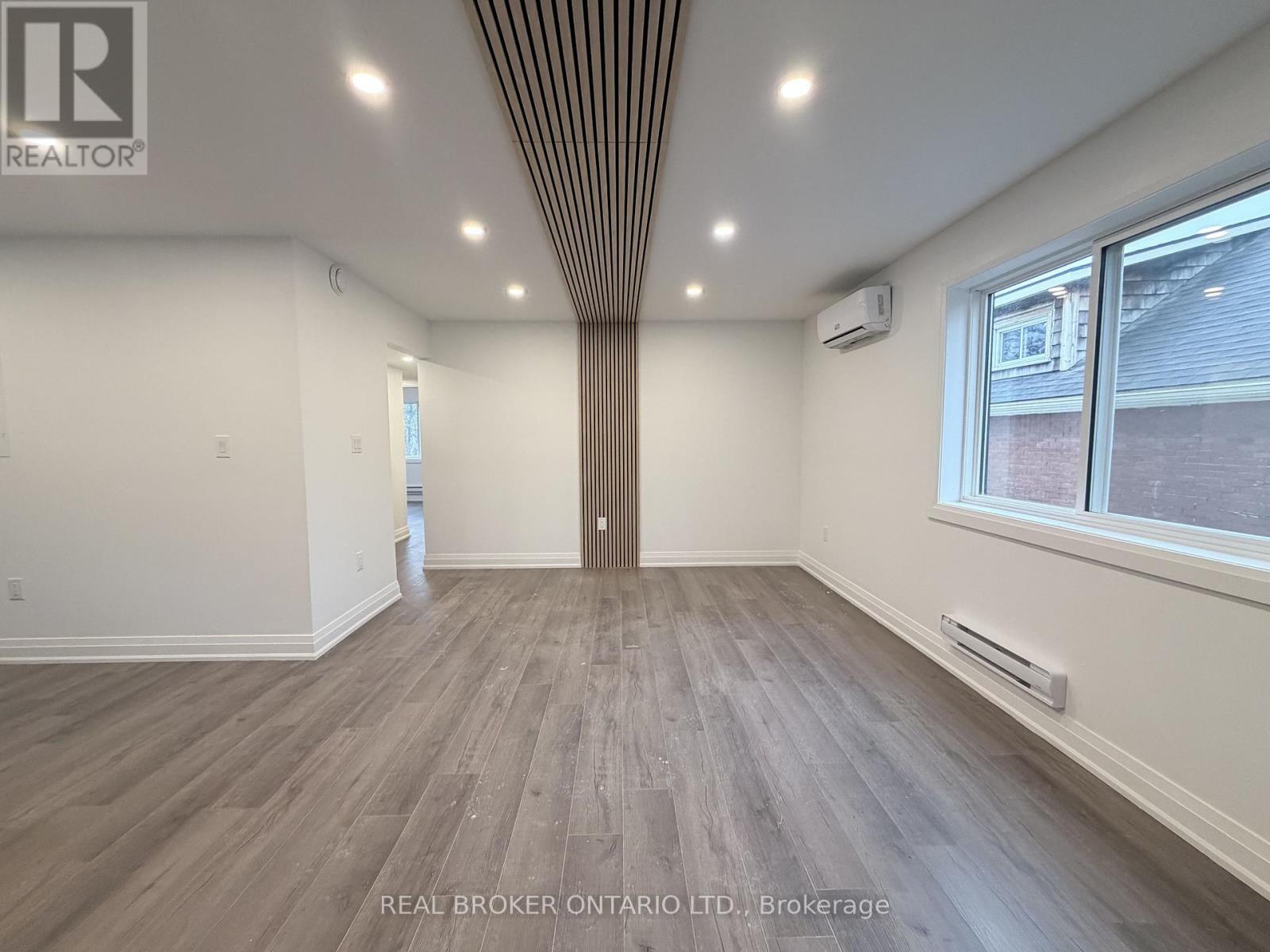 A spacious room with wood flooring and a ceiling with recessed lighting.