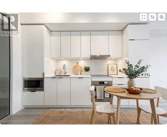A modern kitchen with white cabinets and a dining table set with a bowl of fruit.