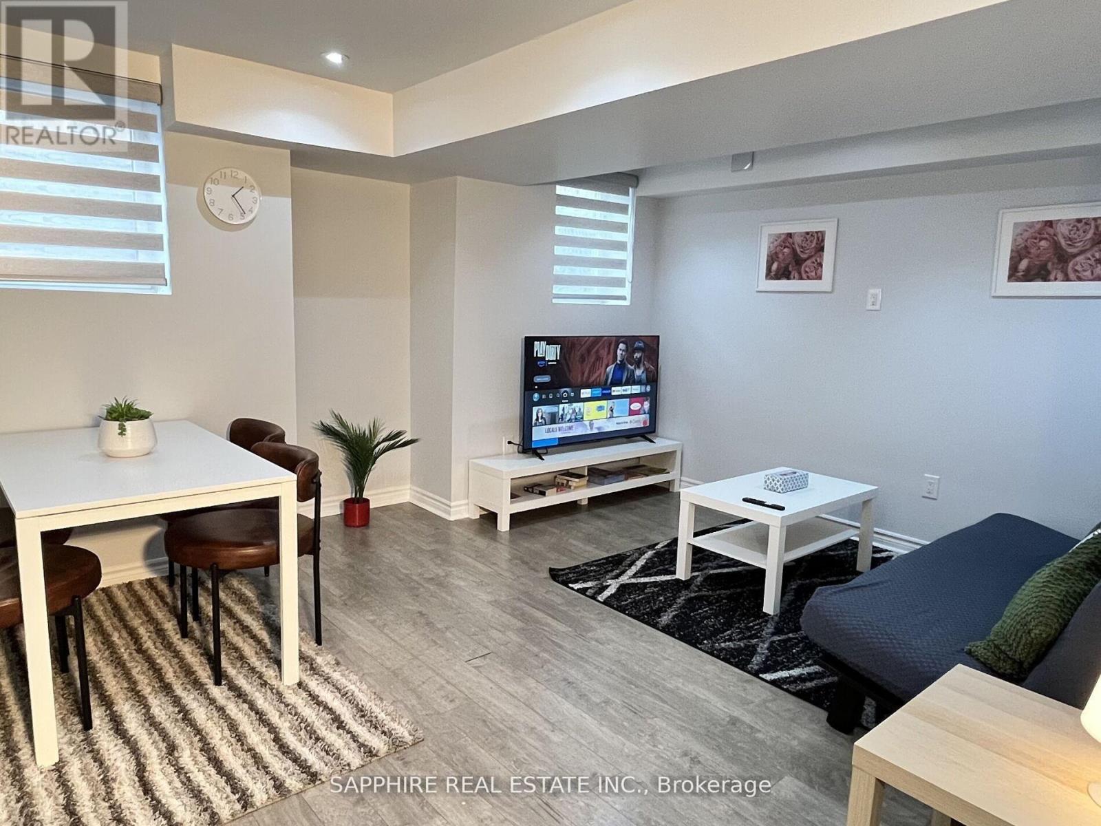 A living room with a white table and chairs, a flat screen TV, and a couch.