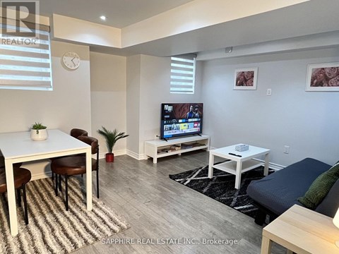 A living room with a white table and chairs, a flat screen TV, and a couch.