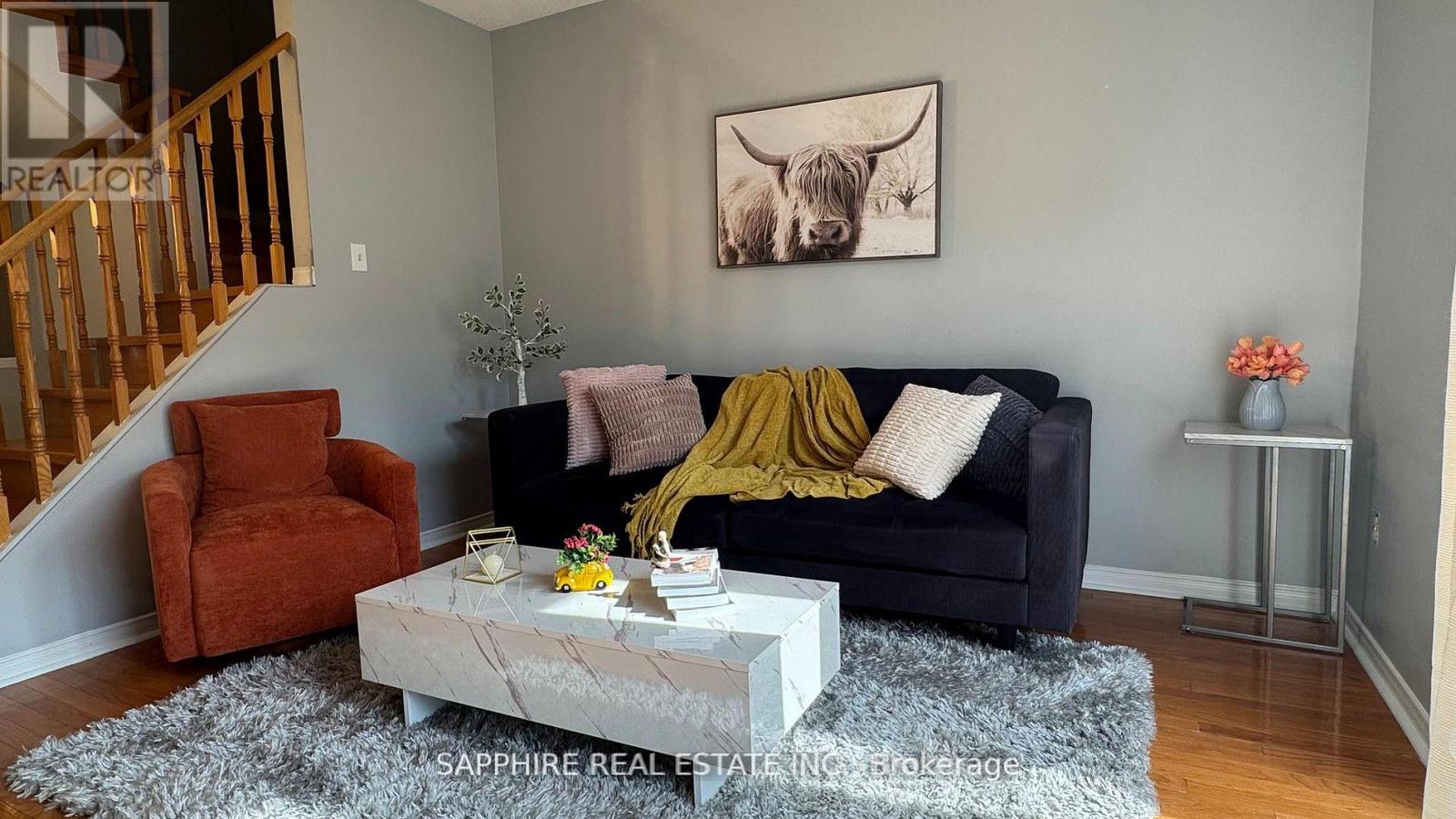 A living room with a black couch, a coffee table, and a painting of a cow on the wall.