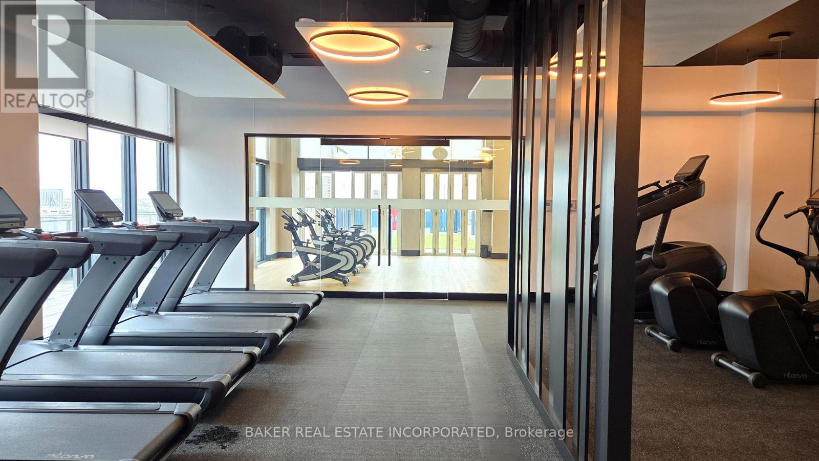 A gym with treadmills and a sign for Baker Real Estate Incorporated.
