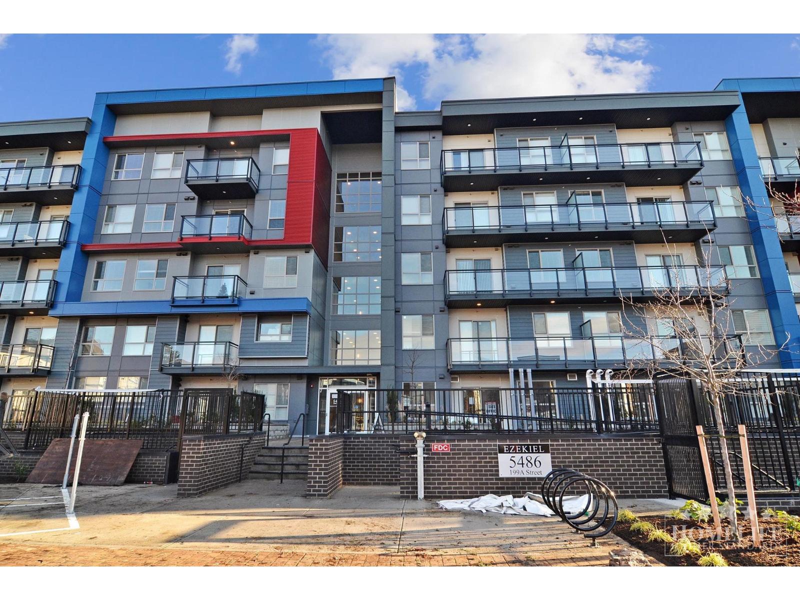 A modern apartment building with balconies and a black fence in front.