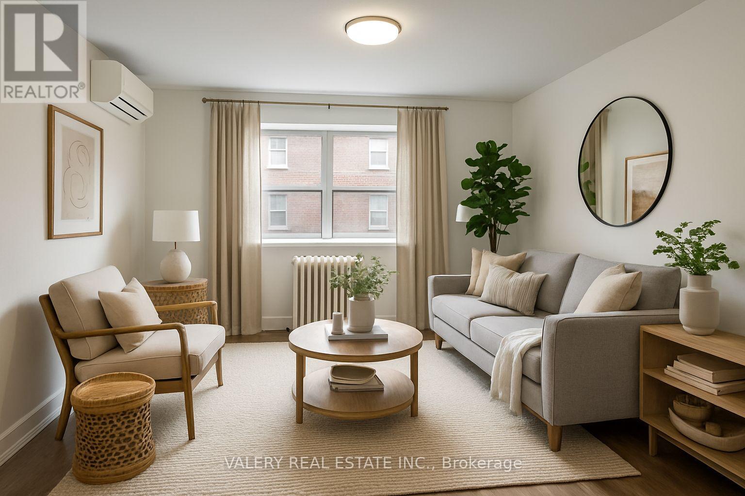 A living room with a grey couch, a wooden coffee table, a chair, a potted plant, and a round mirror on the wall.