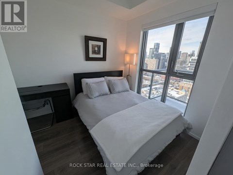 A bedroom with a large bed and a city view through the window.