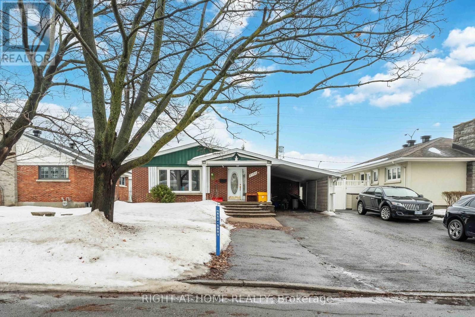 A house with a tree in front and a car parked in the driveway.