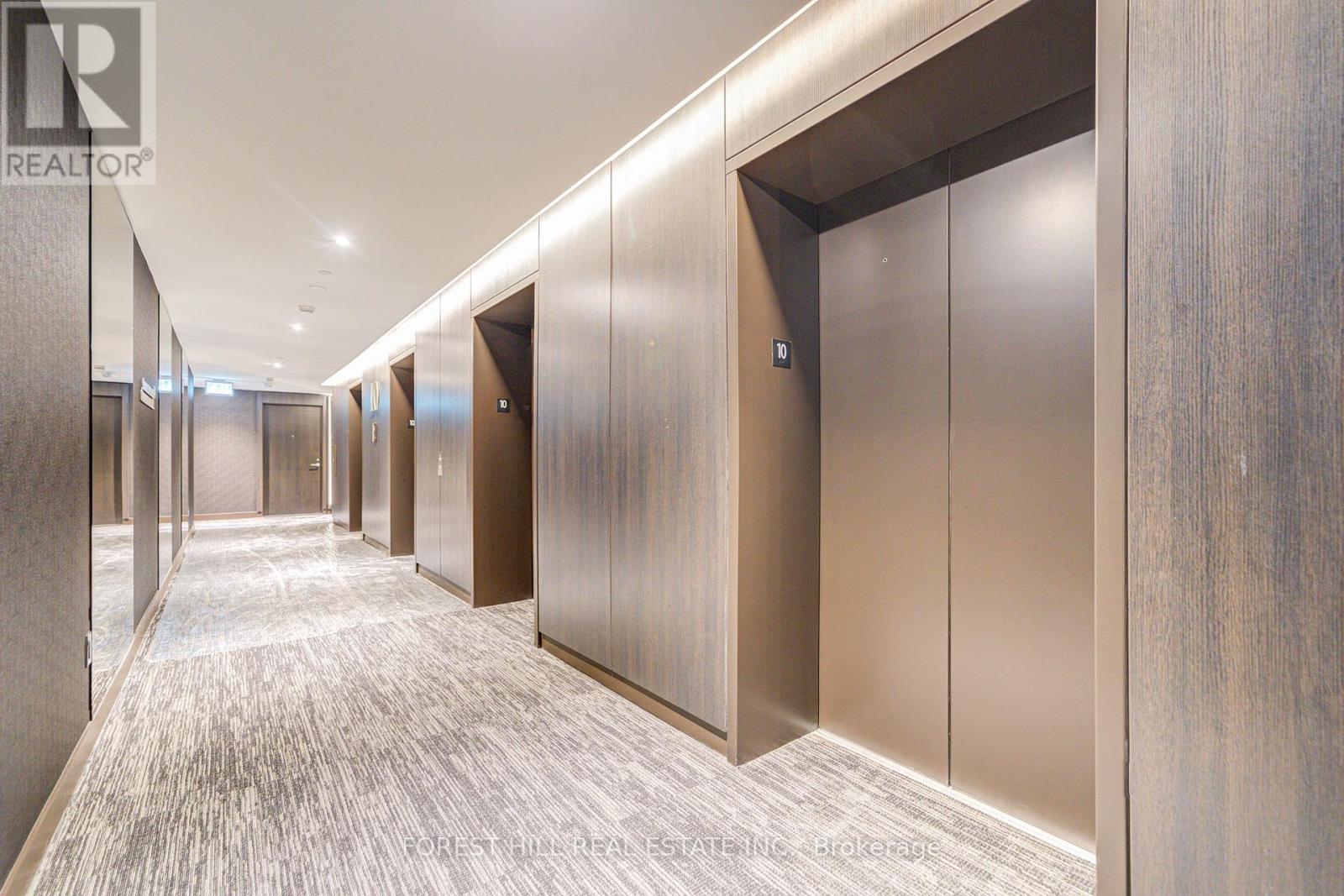 A hallway with a carpeted floor and a row of elevators on the right side.
