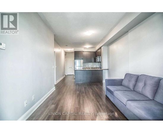 A living room with a grey couch and a kitchen in the background.