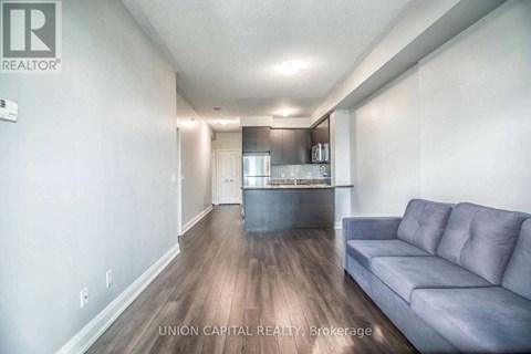 A living room with a grey couch and a kitchen in the background.