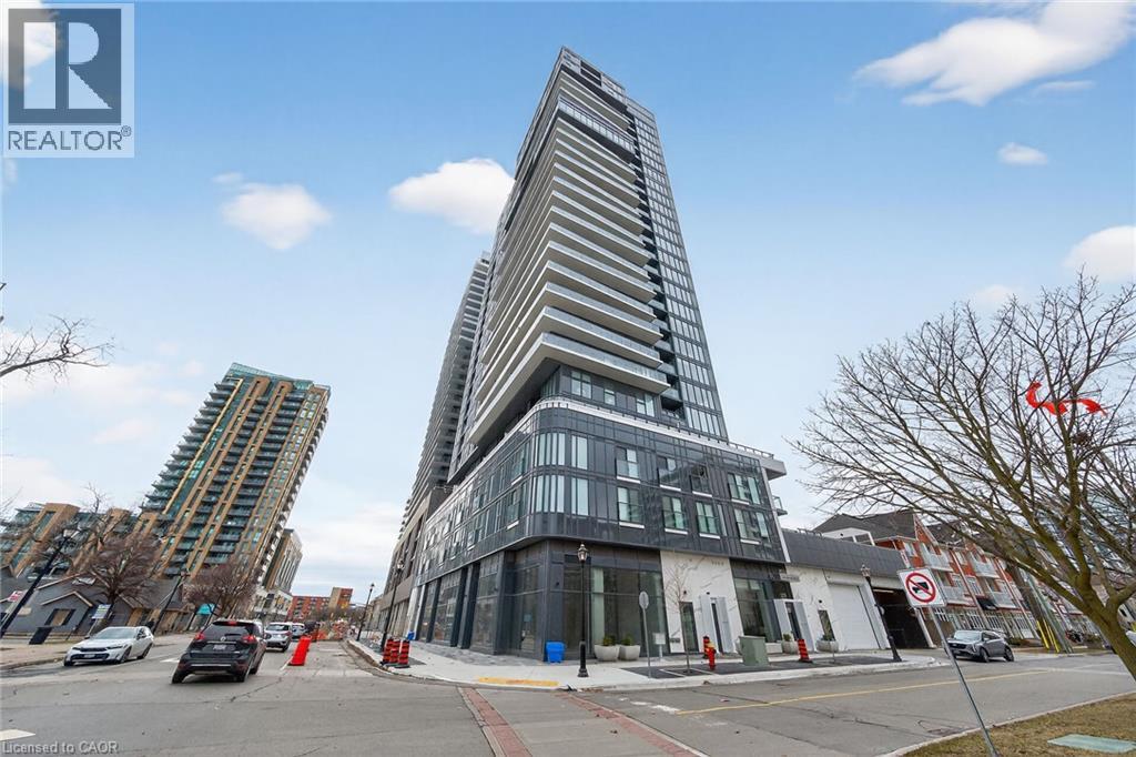 A tall building with a curved facade stands in front of a street with cars and other buildings.