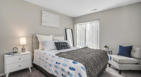 A bedroom with a bed, nightstand, and chair.