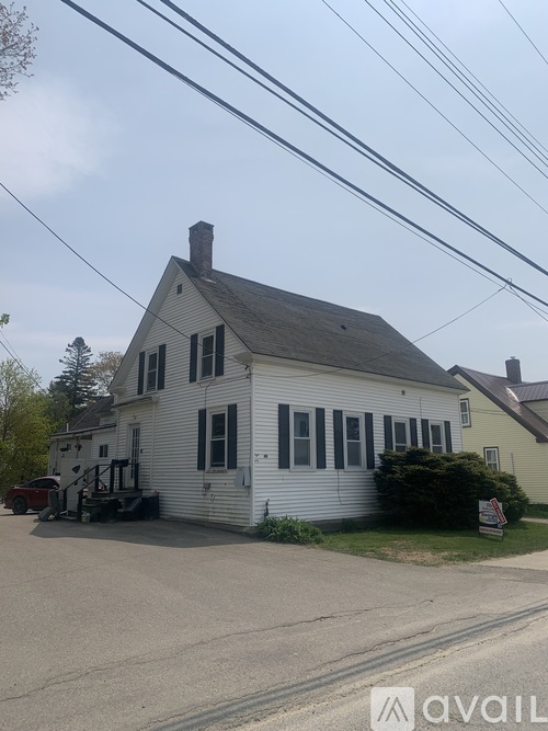 A white house with a grey roof and a chimney is in front of a yellow house.