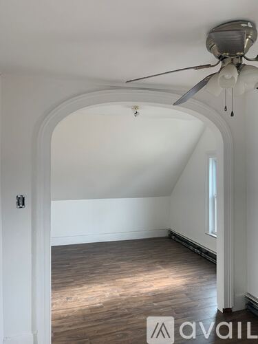 A room with a fan and wooden flooring.