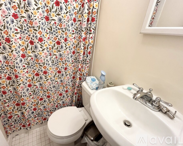 A bathroom with a floral shower curtain, toilet, and sink.