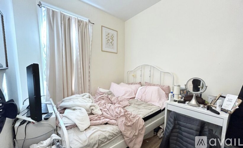 A messy bedroom with a bed covered in pink bedding and a TV on the left.