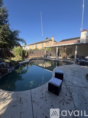 A pool with a stone border and a house in the background.