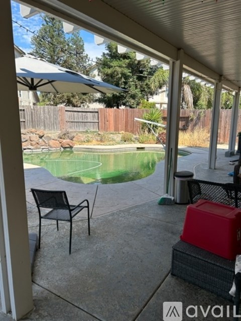 A patio with a chair and an umbrella overlooking a pool.