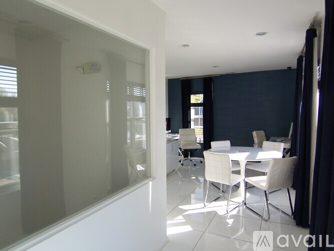 A white dining table with chairs is in a room with a glass wall.