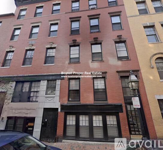A red brick building with a black awning and a sign that says "available" in the foreground.