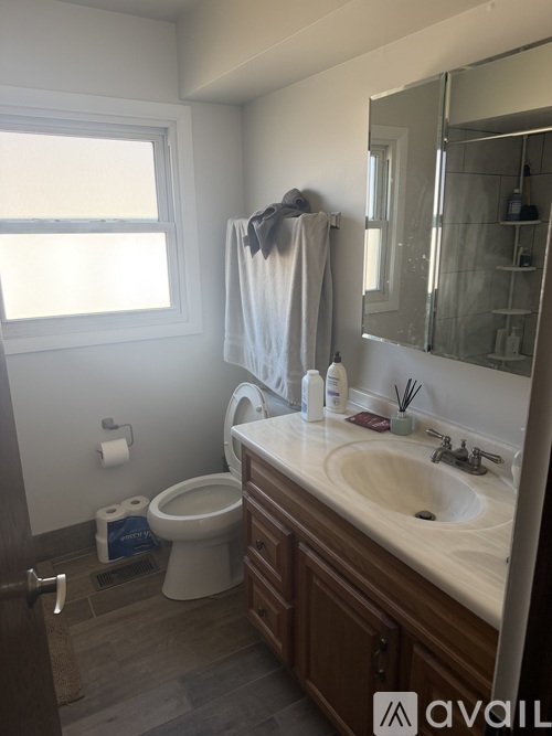 A bathroom with a toilet, sink, mirror, and a window.