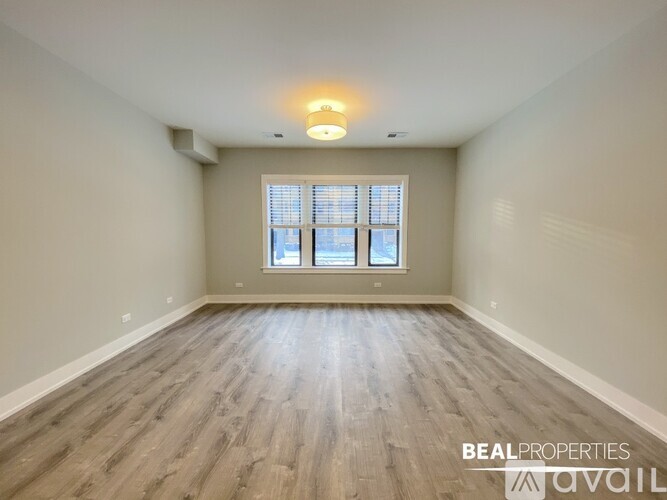 A spacious room with wooden flooring and a window with blinds.