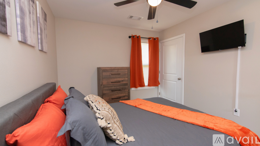 A bedroom with a grey bed and orange pillows.