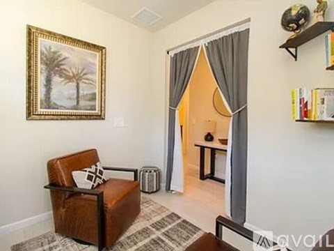 A living room with a brown leather chair and a painting of a palm tree on the wall.