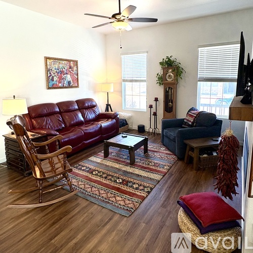 A living room with a red leather couch, a wooden rocking chair, and a rug with a pattern of red, blue, and beige.