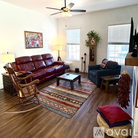 A living room with a red leather couch, a wooden rocking chair, and a rug with a pattern of red, blue, and beige.