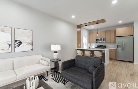 A modern living room with a grey couch and a kitchen in the background.