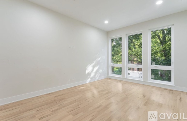 A room with wooden flooring and white walls, with windows showing a view of trees and a building.