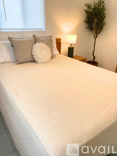 A white bed with a white pillow and a white round pillow on it.