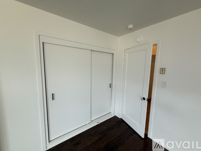 A room with white walls and a wooden floor with a white door and a white cupboard.