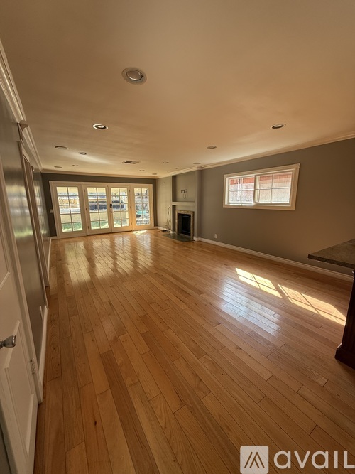 A spacious room with wooden flooring and a refrigerator on the left side.