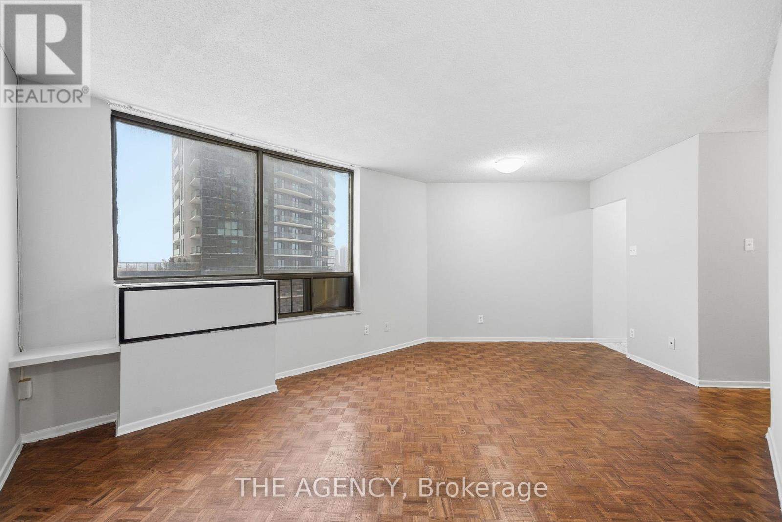 A spacious room with wooden flooring and a large window overlooking a cityscape.