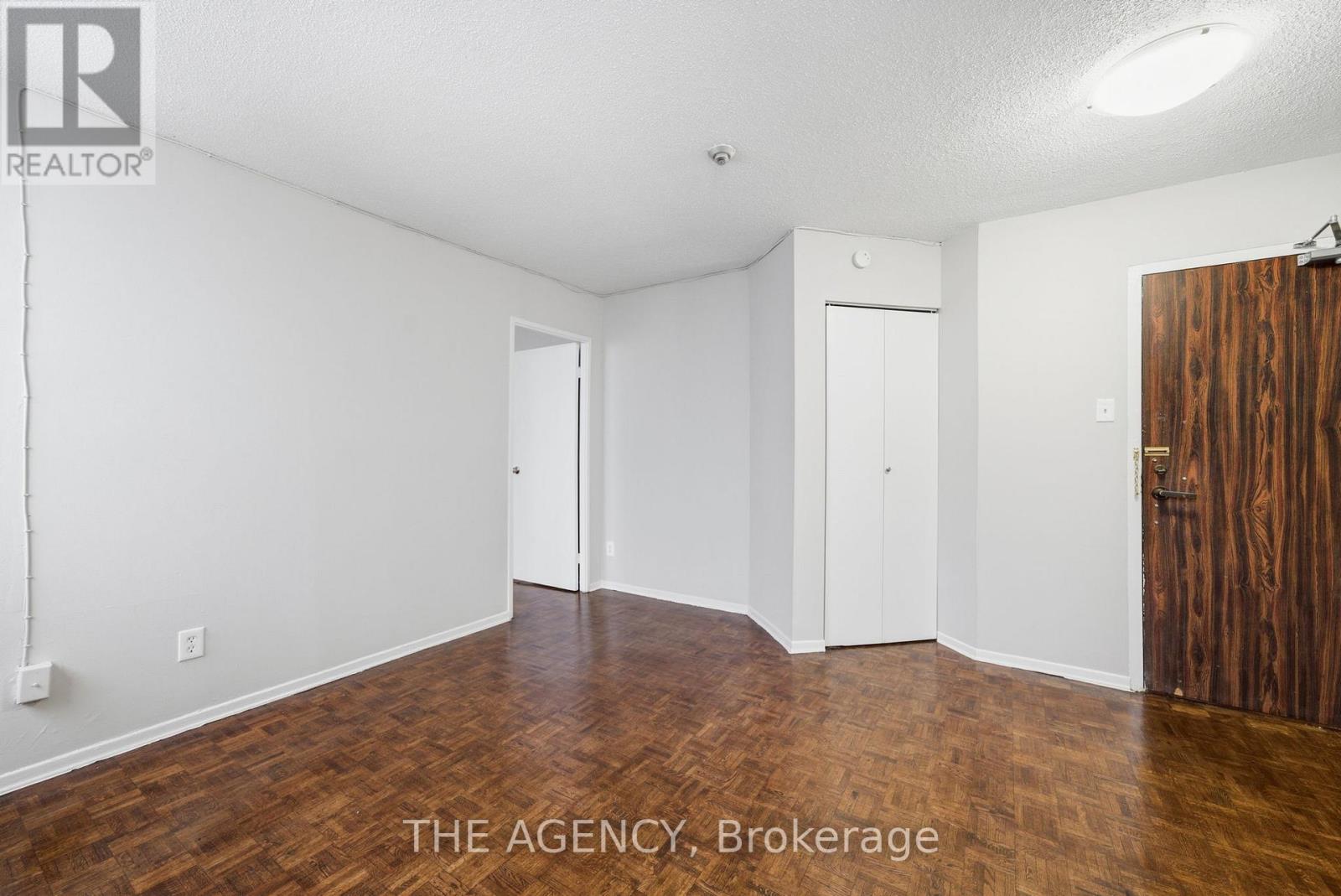 A room with white walls and wooden flooring, with a door on the right and a window on the left.